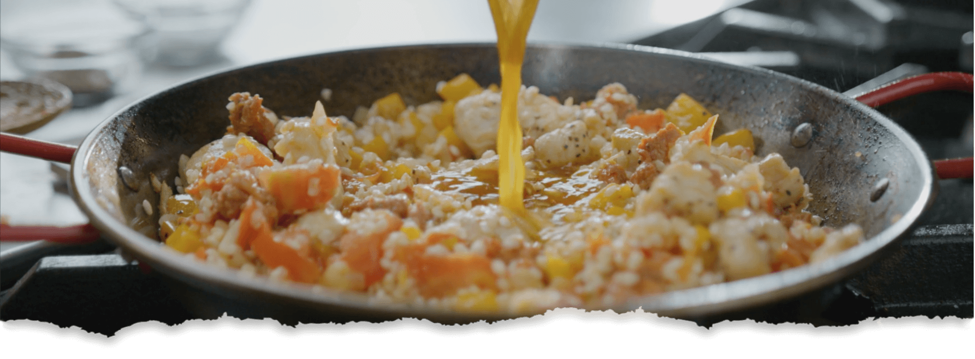 A close-up of a pan, filled with a variety of stir-fry ingredients, including chopped vegetables and an egg being poured.